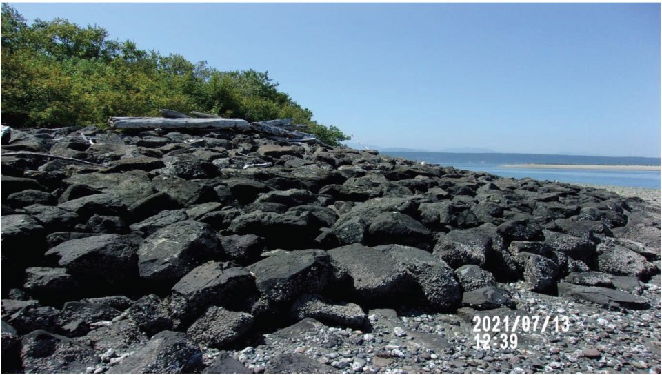 Photograph of beach area showing dark rock protecting the shoreline