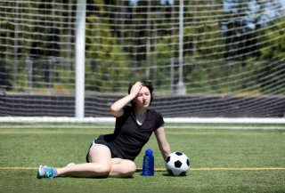Teen girl wipes sweat off her brow, while sitting on a soccer field.