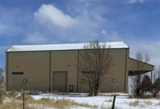 Photograph of a steel building with a few trees and snow cover on the ground