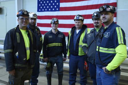Six miners posing in front of the American flag.