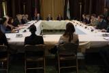 Numerous people sit around a large, square conference table