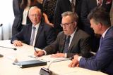 Acting EPA Administrator Andrew Wheeler sits at a table and signs a paper as two other men look on