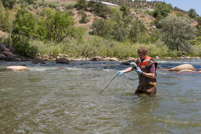 a man holding a electronic measuring device and a water probe, standing waist-deep in the middle of a river