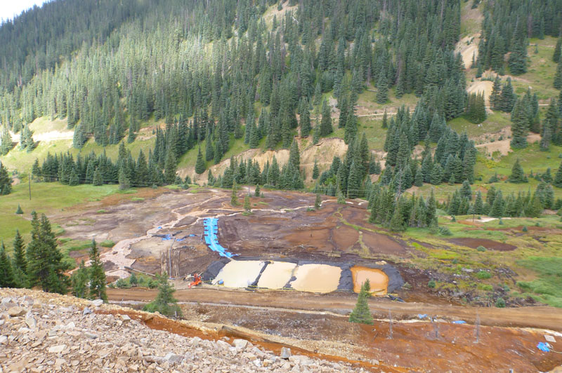 Looking down into a forested valley, with four large, square constructed ponds and drainage channels.