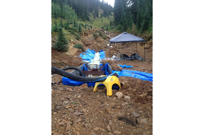 A narrow, forested valley with machinery and pump hoses with a drainage ditch lined with plastic sheets.