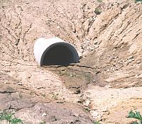 Photo of a drain pipe nearly buried from the hillside gravel and sand running down on it.