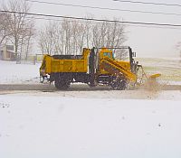 Photo of a snowplow applying rock salt on the road during a snowstorm.