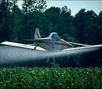 Photo of a crop duster airplane spraying agricultural fields with pesticides.
