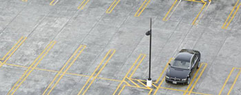 Photo of a parking lot with one black car by a street light.