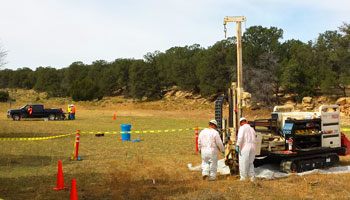 Hardhat workers standing next what appears to be a mobile drilling rig