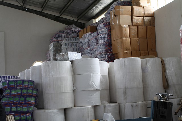 This is an image of paper and paperboard materials in a storage area. The materials are stacked, some reaching close to the ceiling.