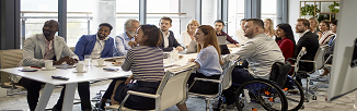 A group of professionals of varying ethnicities and gender seated at a conference table and looking towards something out of frame