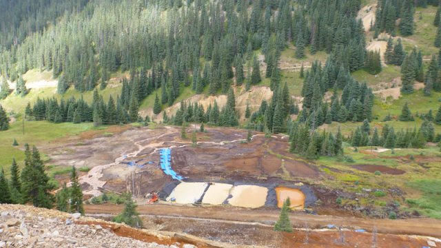 Looking down into a forested valley, with four large, square constructed ponds and drainage channels.