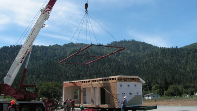 Manufactured home being lifted off of a flatbed with a crane for installation on site.