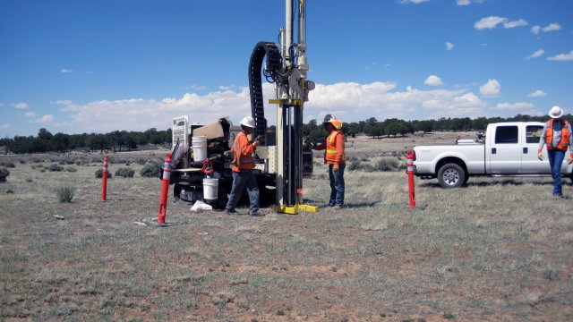 Hardhat workers standing next what appears to be a mobile drilling rig.