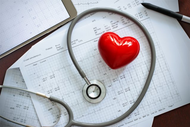 A stethoscope around a toy heart on top of charts