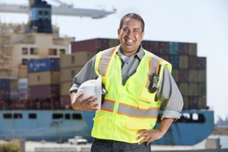 A photo of a man standing in the foreground with a container ship in the background.