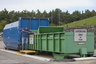 This is a photo of a worker using a tool to sort cardboard in a large collection bin.