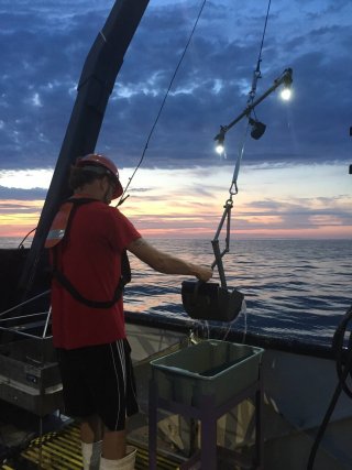 Photo of marine technician collecting sediment from a Ponar sampler