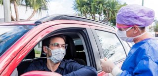 Man giving a health care worker a test swab while sitting in a car