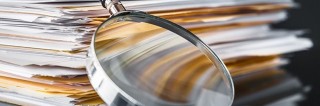 Image of a magnifying glass leaning against folders with papers.