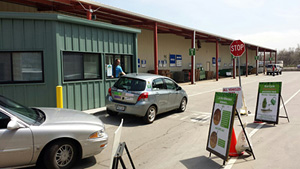 Center for Hard to Recycle Materials (CHaRM) drop off area in Boulder, CO. Cars lined up to pass by booth. Driver is speaking to booth attendant. Warehouse in the background.