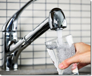 A hand filling a clear glass with water from a sink faucet