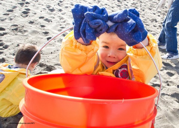 Photo of kid with bucket cleaning up at the beach