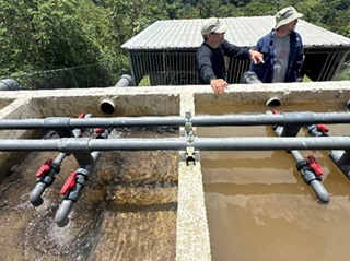 Two men talking behind a pipe water system in a rural outdoor area