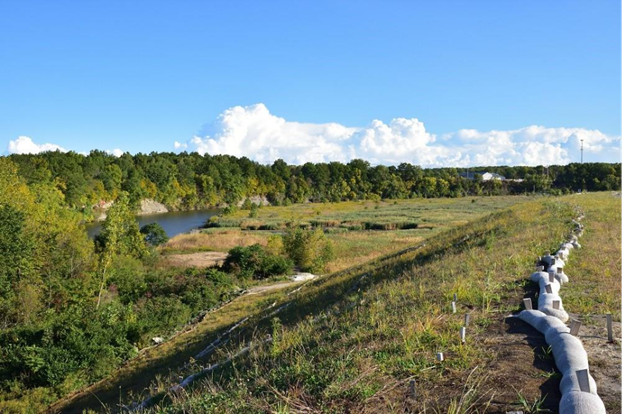 Post-construction view of capped and covered slag adjacent to a restored floodplain wetland along the Black River with established vegetation, and erosion control measures under a clear blue sky with white clouds. 