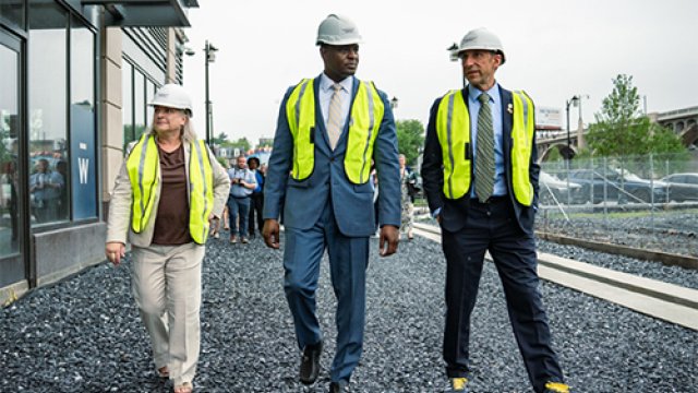 Three people wearing hard hats and fluorescent yellow vests walk on an outdoor job site.