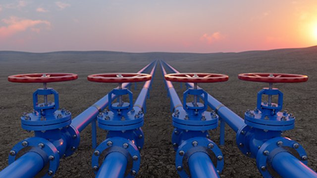 Four blue pipes with round red shutoff valves against a western landscape.