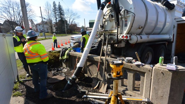 Two workers watch a a high-powered vacuum hose placed inside the culvert to remove sediment 