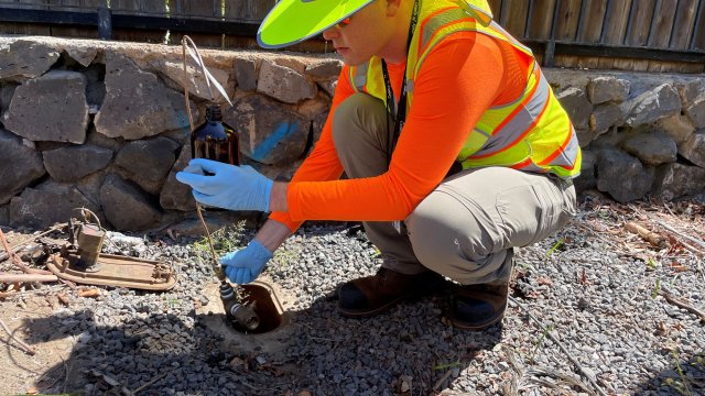 Worker in high visibility vest crouching next to a drinking water access panel taking a water sample.