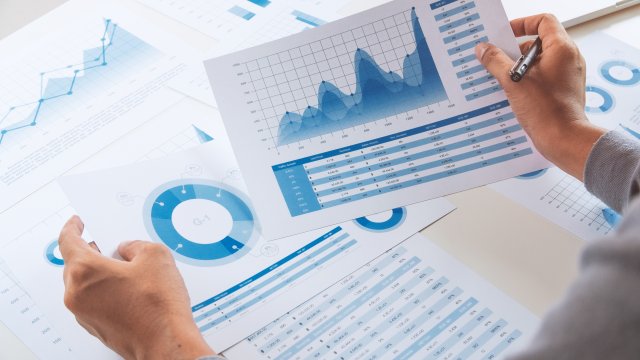 Hands hold papers with graphs and tables printed on them