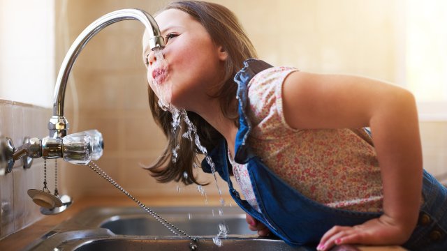 A little girl drinking water directly from the kitchen tap at home.