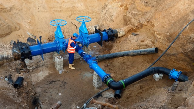 Technical expert open gate valve on 500mm drink water pipes joined with black multi joint members into old pipeline system.