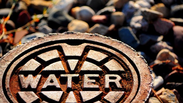 Water supply access point, rusty sewer cover on ground, public utility on road of rock ground in city