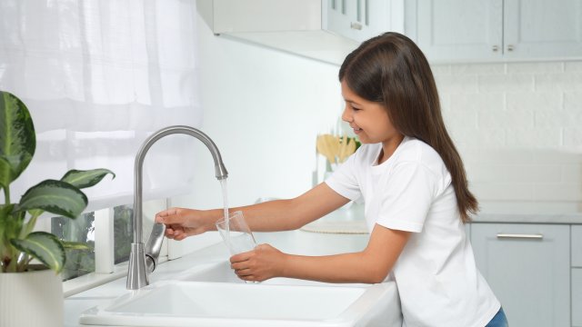 Girl filling glass with water from tap in kitchen