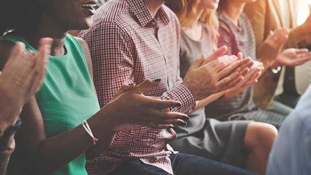 People sitting a row, clapping with happy expressions on their faces