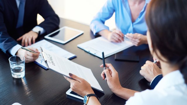 three people sitting at a table with note pads and tablets