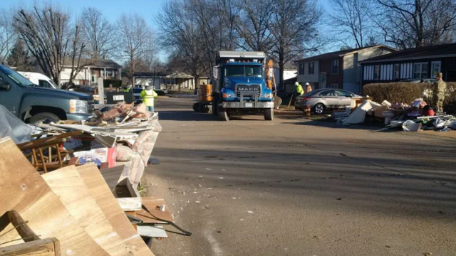 truck driving down a street lined with disaster debris