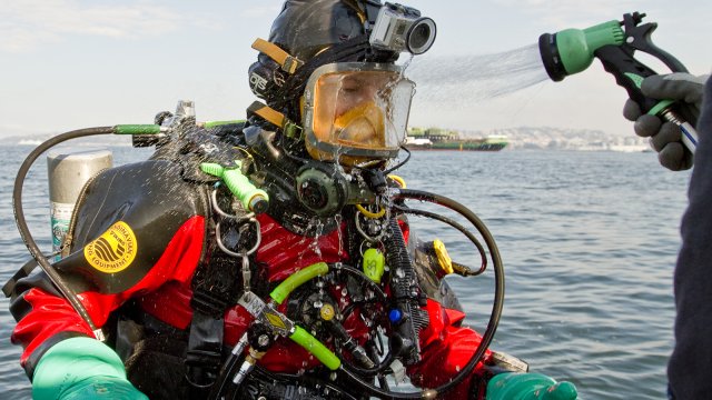 EPA diver in full SCUBA gear being sprayed with clean water after a polluted water dive.