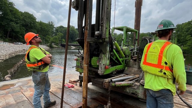 The image shows construction crew members using equipment to collect sediment samples.