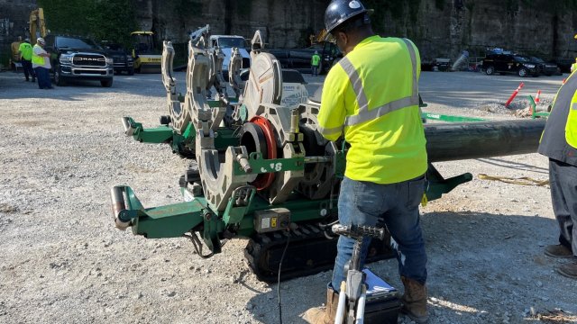 The image shows a construction crew member using equipment on a large pipe. 