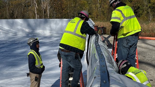Construction workers install liner on tank.