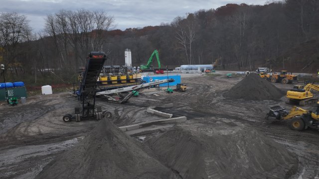 Black piles of material in front of conveyor belt and next to construction equipment. 