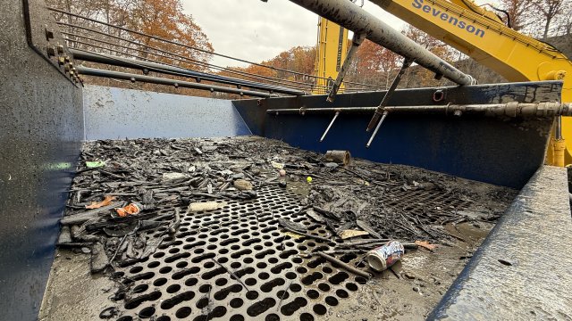 Sticks and trash sit on top of a plate with large holes in it. An arm for an excavator is in the background. 