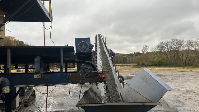 Equipment on the left feeds material onto a conveyor belt in the center of the image. 