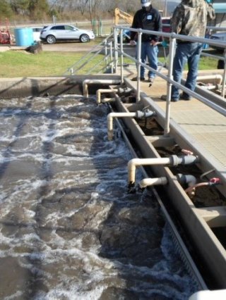 While standing above an aeration basin the compliance advisor discusses operations with the wastewater system operator.